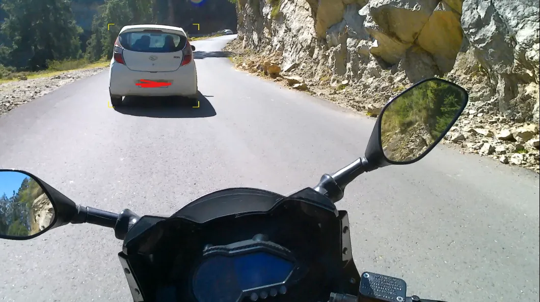 A white hatchback ahead on a narrow mountain road, marked with small yellow corner brackets.