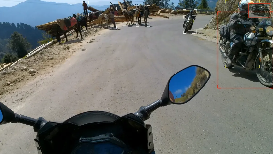 A loaded mule train in the distance and a rider on a motorcycle close on the right, who is outlined in red, with a small marker on a far vehicle.